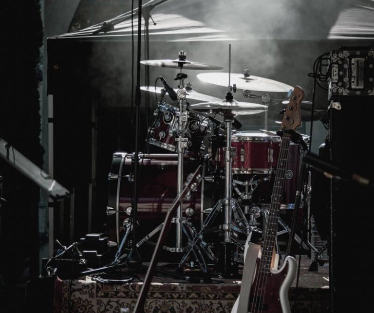 Dimly lit stage with drum kit and electric guitar ready for a live performance.