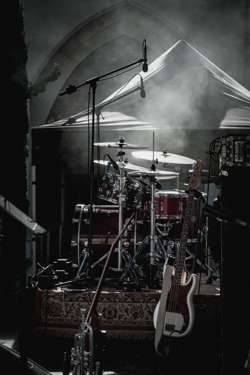 Dimly lit stage with drum kit and electric guitar ready for a live performance.