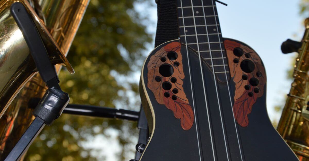A colorful ukulele alongside brass instruments like saxophones, displayed outdoors in natural light.