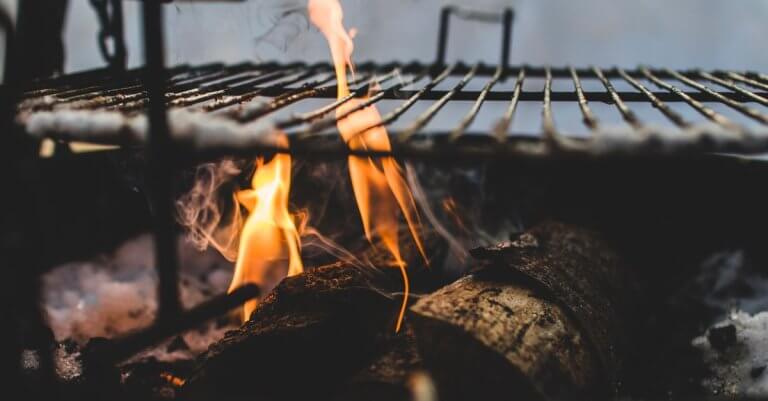 Close-up view of firewood burning in a fire pit with a metal grill above, outdoor setting.